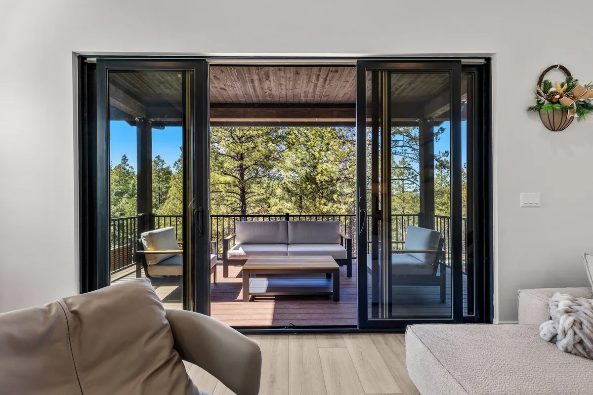 Large sliding glass doors open onto an outdoor seating area, with views of surrounding trees and a tranquil deck space. The scene blends indoor comfort with the inviting presence of nature, offering the perfect spot for sunrise coffee or evening stargazing.