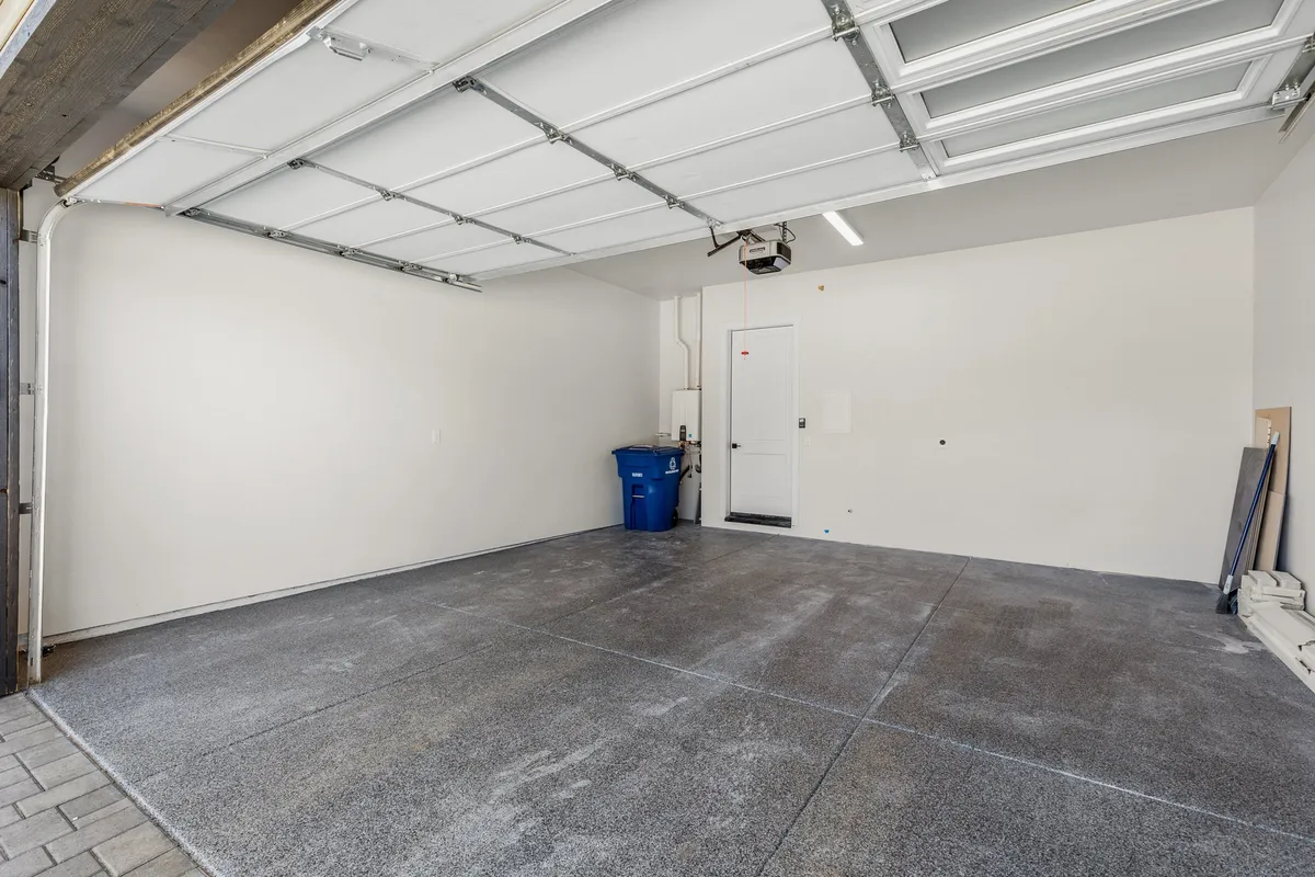 A practical, organized garage space featuring a garage door, blue trash bin, and a convenient side door, emphasizing secure storage and easy access for gear and vehicles.