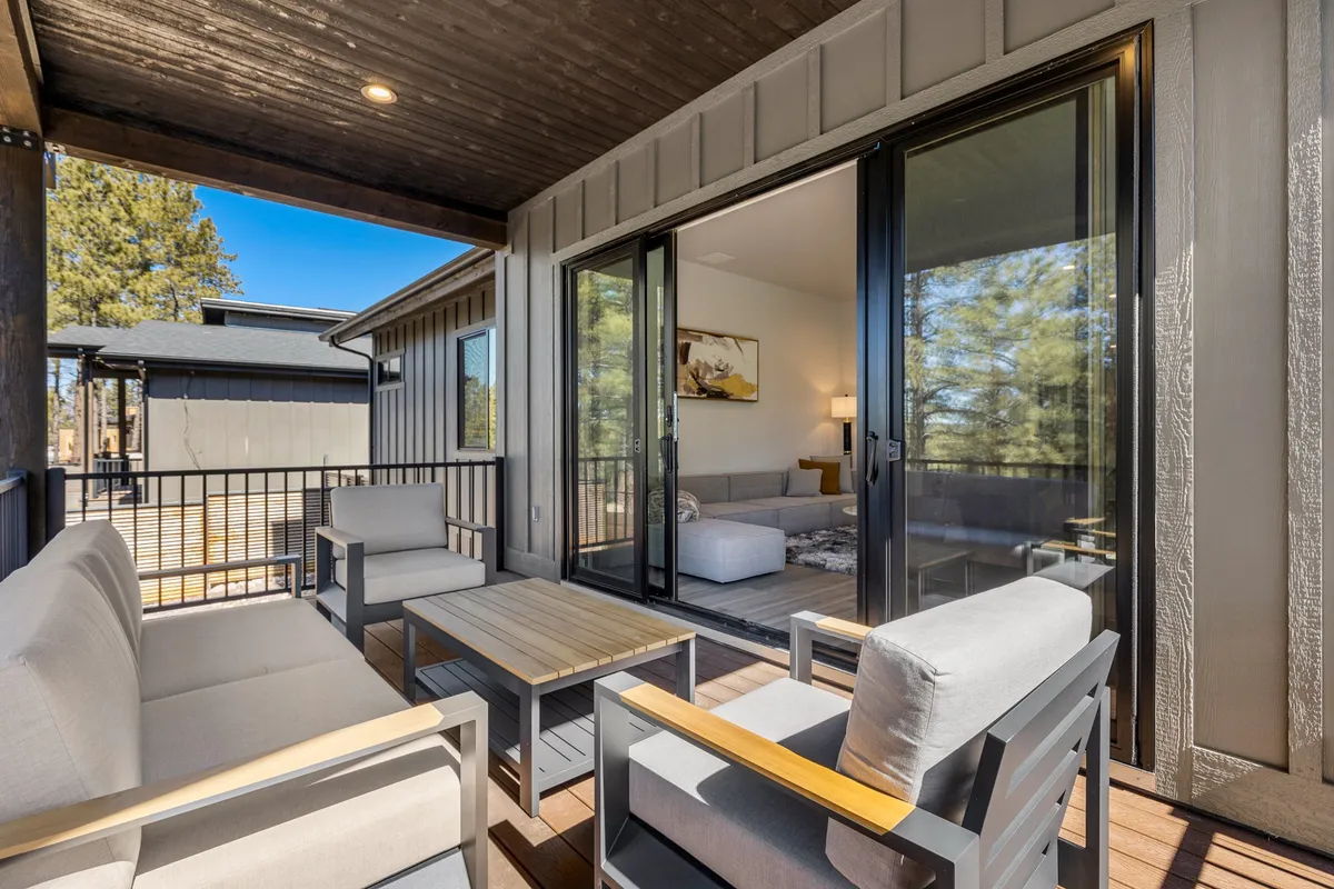 A tranquil outdoor deck with comfortable seating, surrounded by trees and accessible through sliding glass doors, offering a seamless transition between indoor and outdoor spaces.