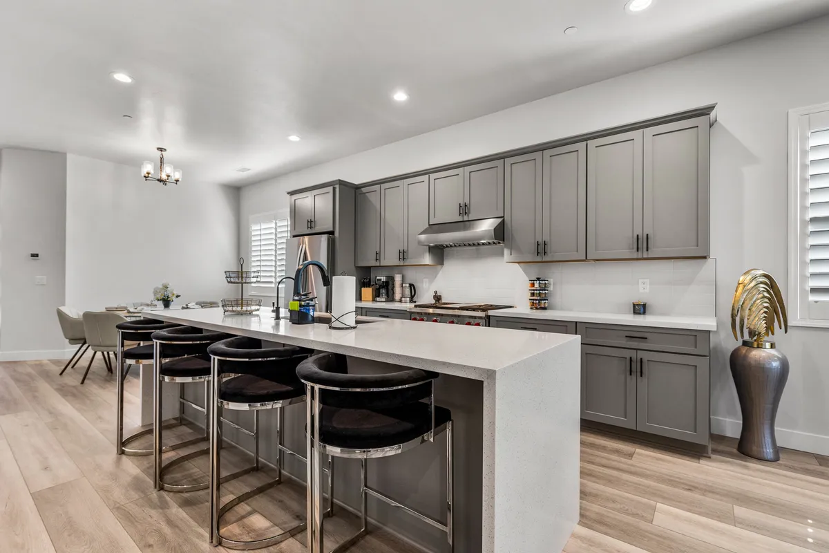 A sophisticated kitchen featuring an island with bar stools, gray cabinetry, stainless steel appliances, and decorative plants. The breakfast bar invites casual conversation and the open layout enables the cook to engage with guests or family during meal prep.