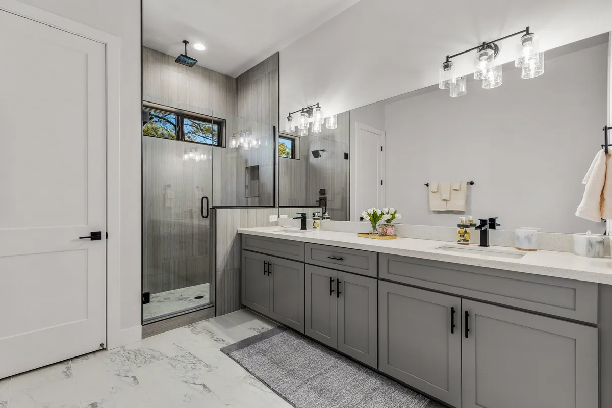 A modern ensuite bathroom with a double sink vanity, glass shower enclosure, and elegant lighting fixtures. The atmosphere is clean, refreshing, and perfect for private self-care routines.