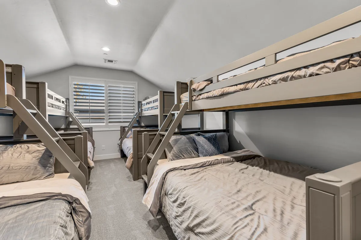 This image showcases a cozy bunk room with bunk beds dressed in comfortable bedding and textured pillows. The setup exudes a communal yet comfortable feel, perfect for children, cousins, or friends eager for late-night chats or storytelling.