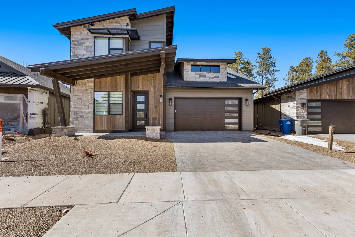 The modern exterior of the property features striking stonework, large windows, and wood accents. The architecture invites gatherings and social moments, with a spacious porch ideal for watching sunsets or hosting barbecues against the beautiful forest backdrop.