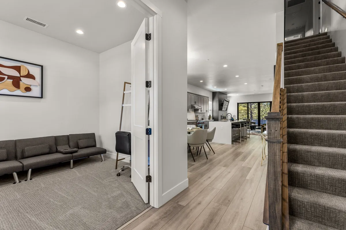 A welcoming living area with a cozy sofa overlooking the kitchen, visible stairs, and artwork on the wall. The space is open and inviting, suggesting a natural flow for groups gathering before or after outdoor activities.