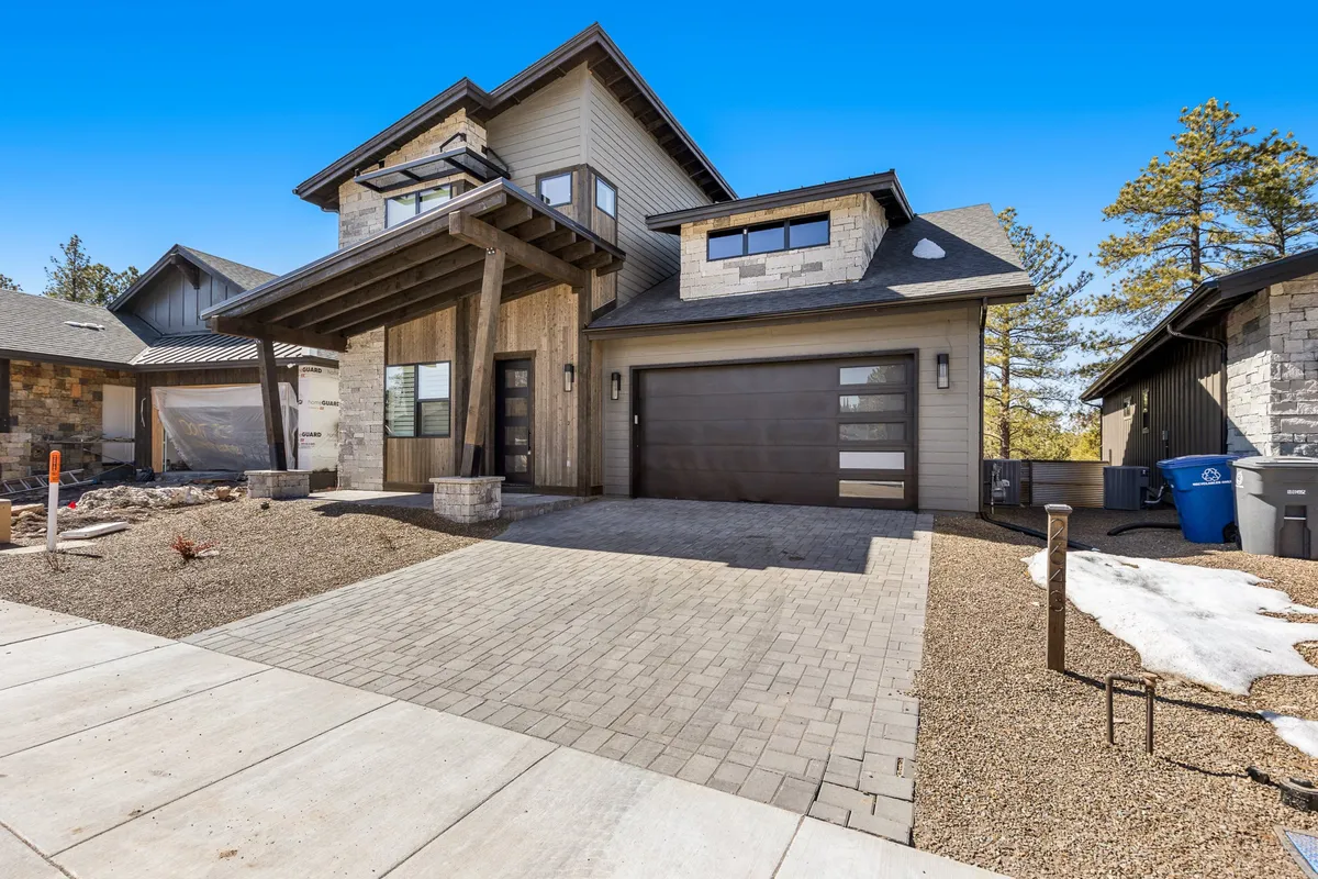 A striking exterior view of the home showcasing its modern architecture, featuring wooden beams, a stone facade, and a welcoming garage door. The front porch and surrounding landscaping hint at spaces for gathering and celebrating outdoors.